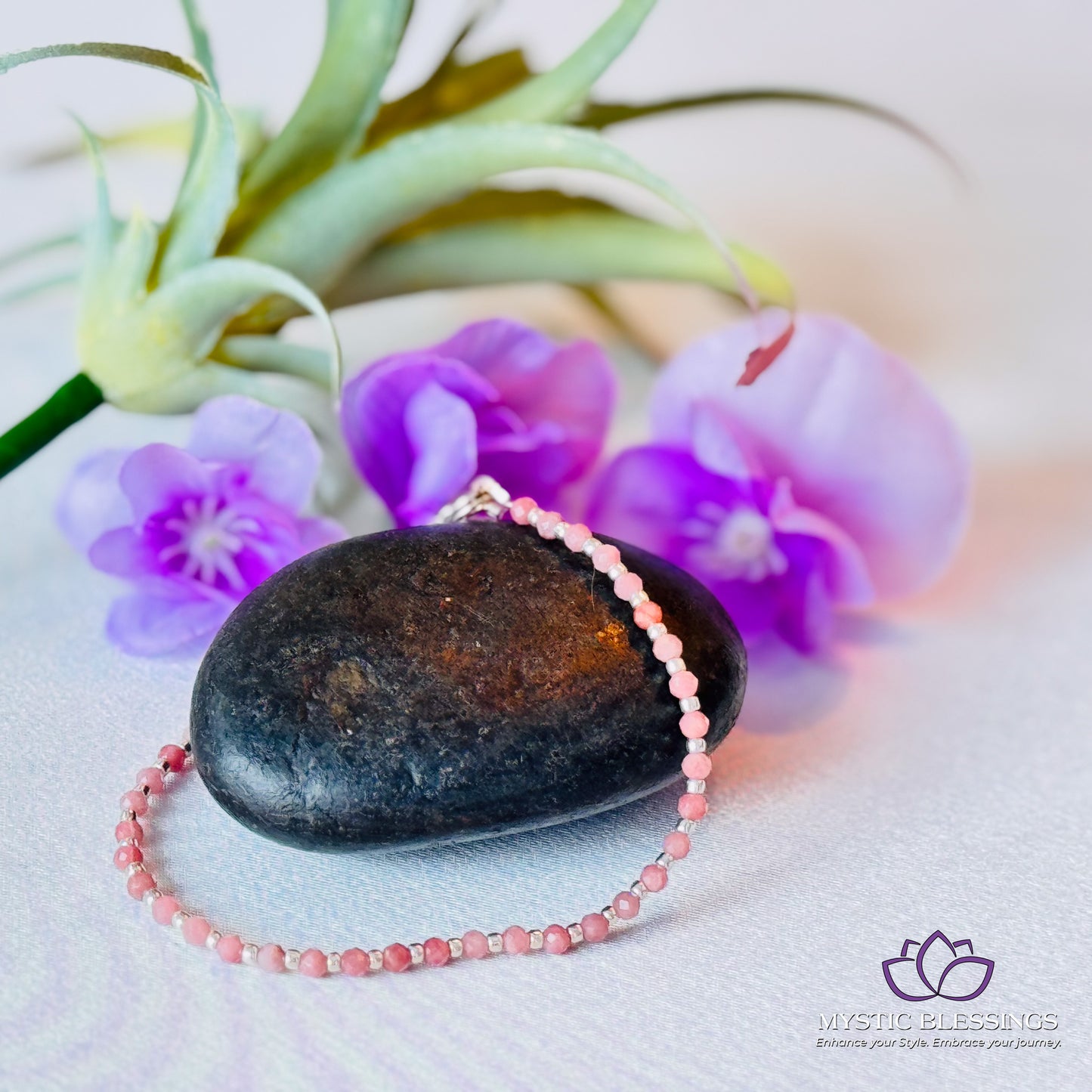 a rock with a pink beaded necklace next to purple flowers