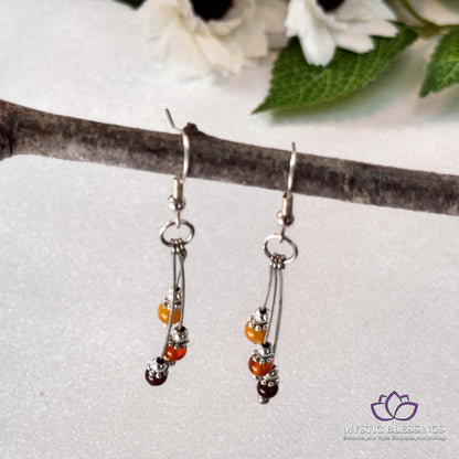 a pair of orange and silver earrings sitting on a branch